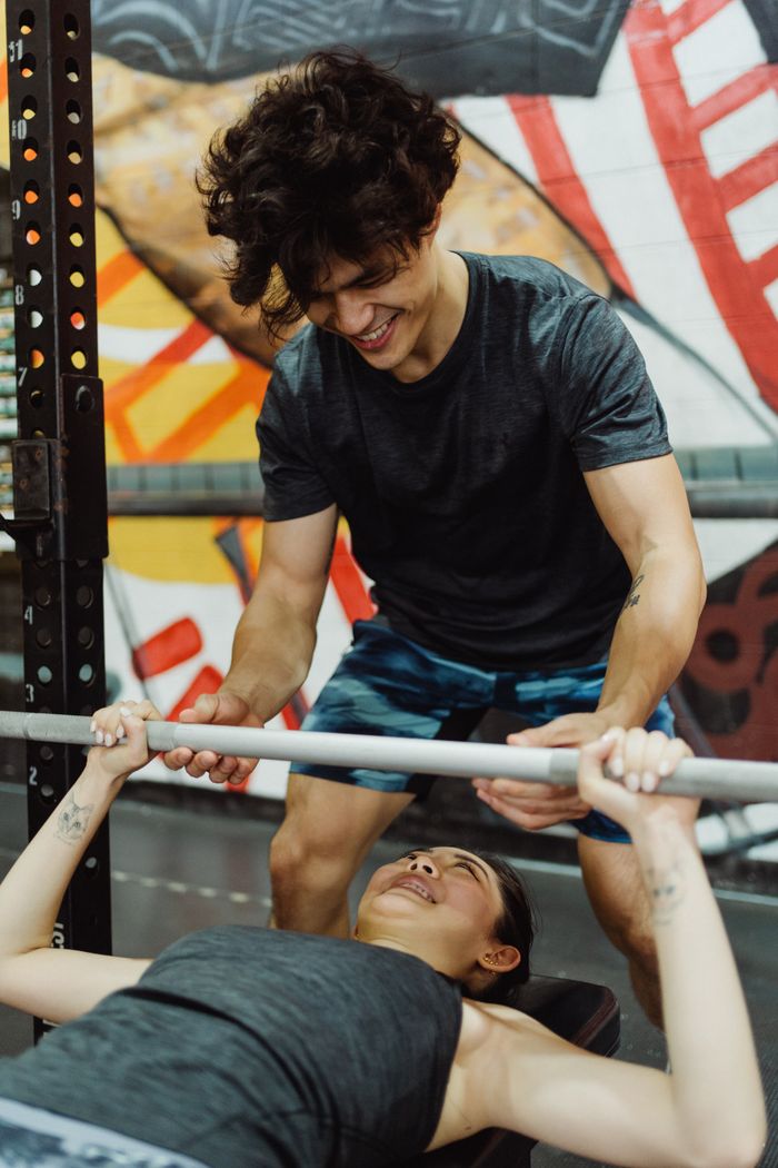 A couple engaged in a workout session, supporting each other while exercising at the gym.